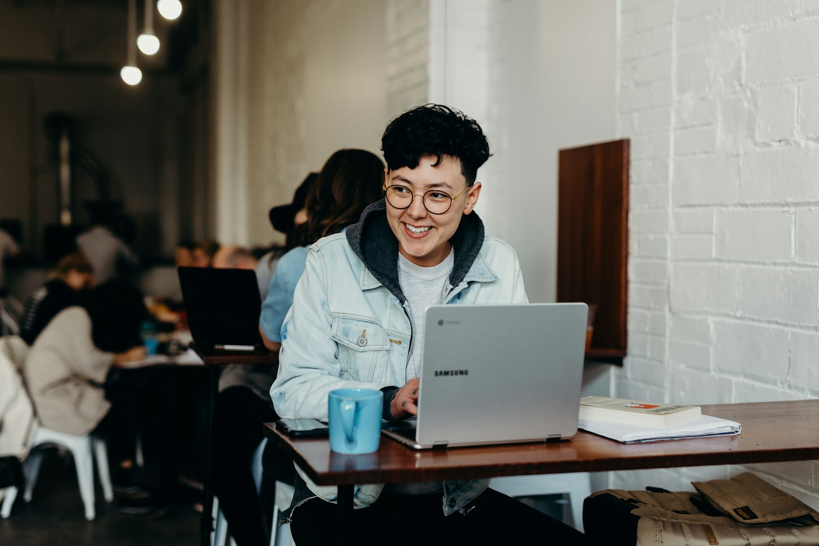 Student smiling at his laptop in a busy cafe
