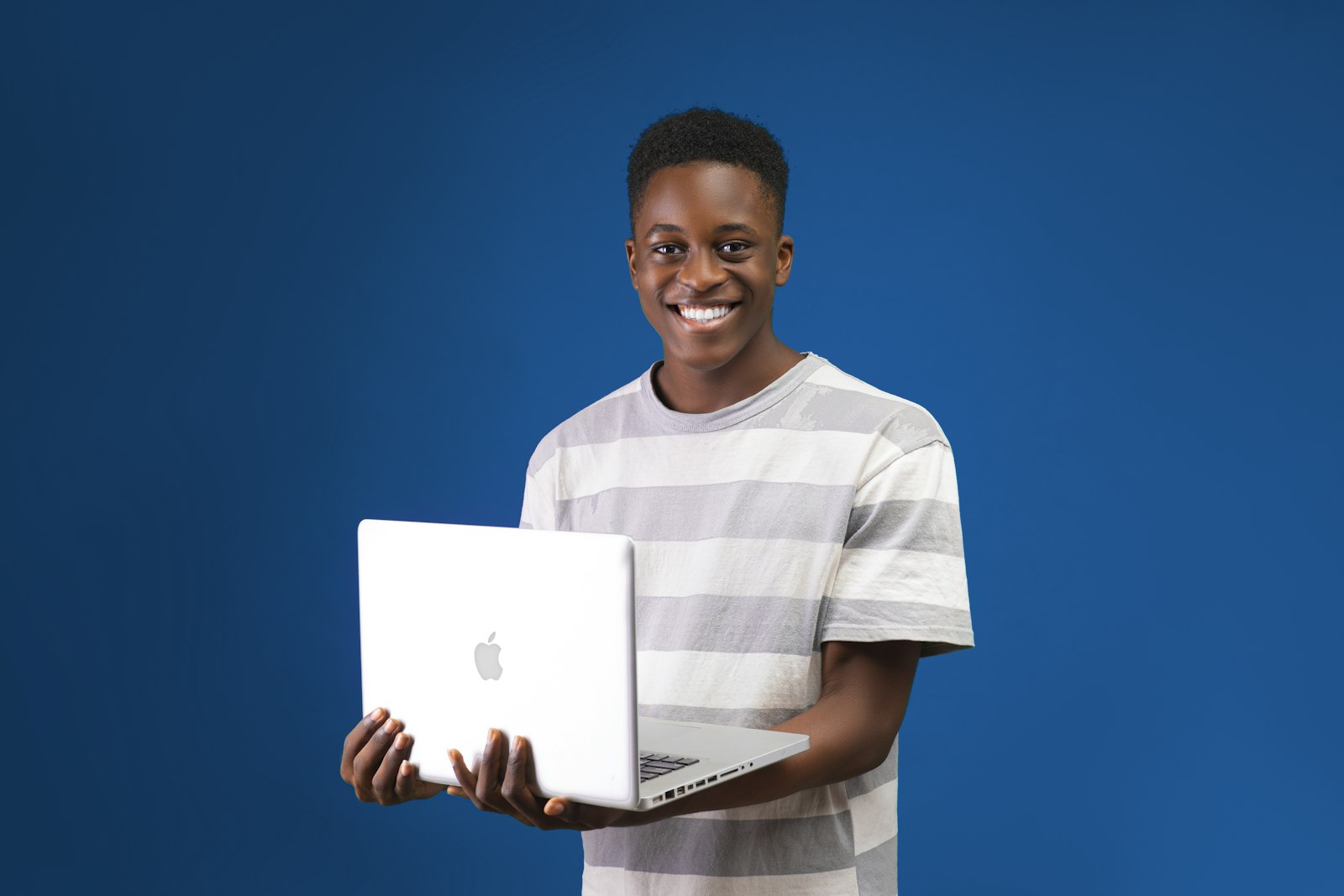 Student smiling and holding a laptop against a blue wall